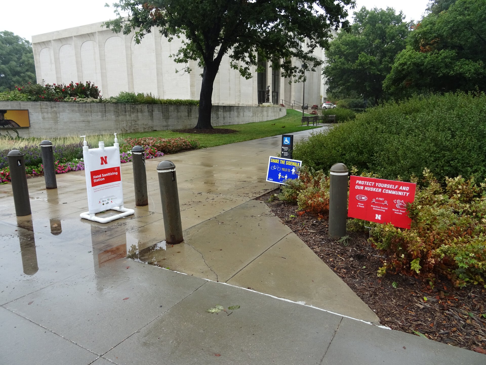 Collection of signs near sidewalk with Sheldon Museum in background.